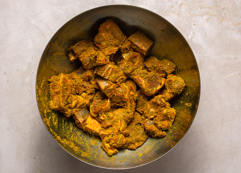 goat meat marinating with green seasoning and curry powder in a bowl