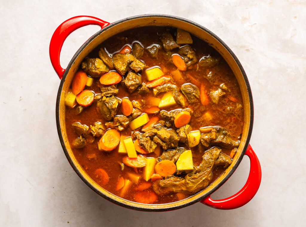 adding potatoes and carrots to braised curry goat