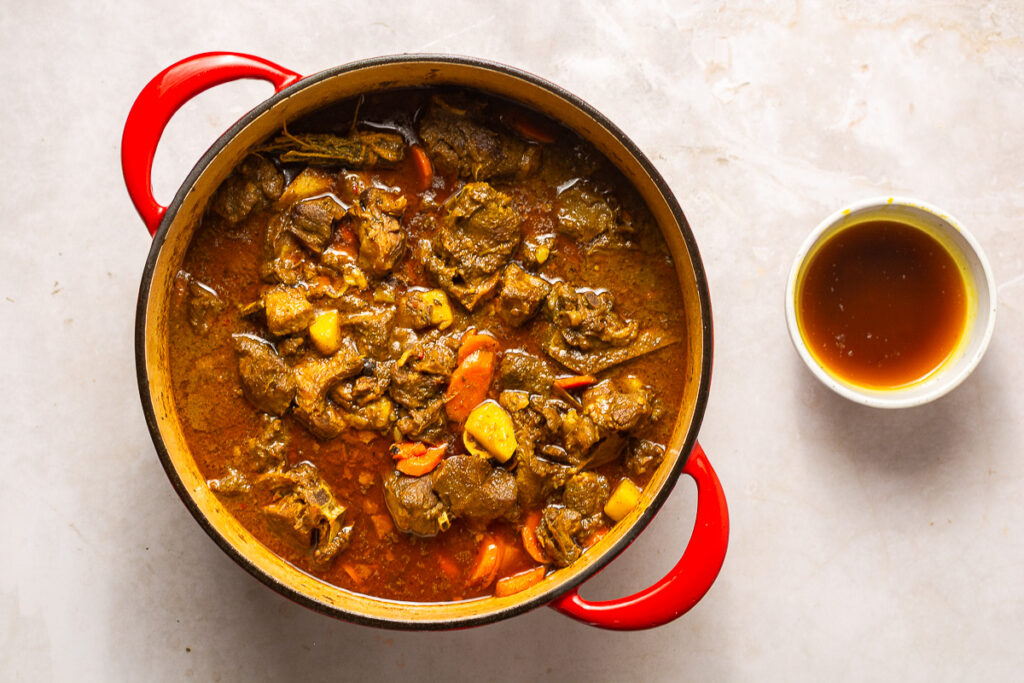 skimming excess fat from Jamaican curry goat
