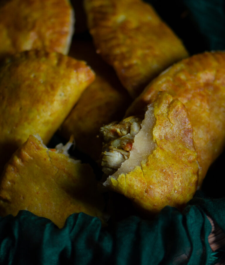 basket filled with homemade Jamaican curry chicken patties with one patty torn open to show curry chicken filling