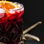 closeup of a glass of Jamaican sorrel drink garnished with a slice of orange and cinnamon stick in glass