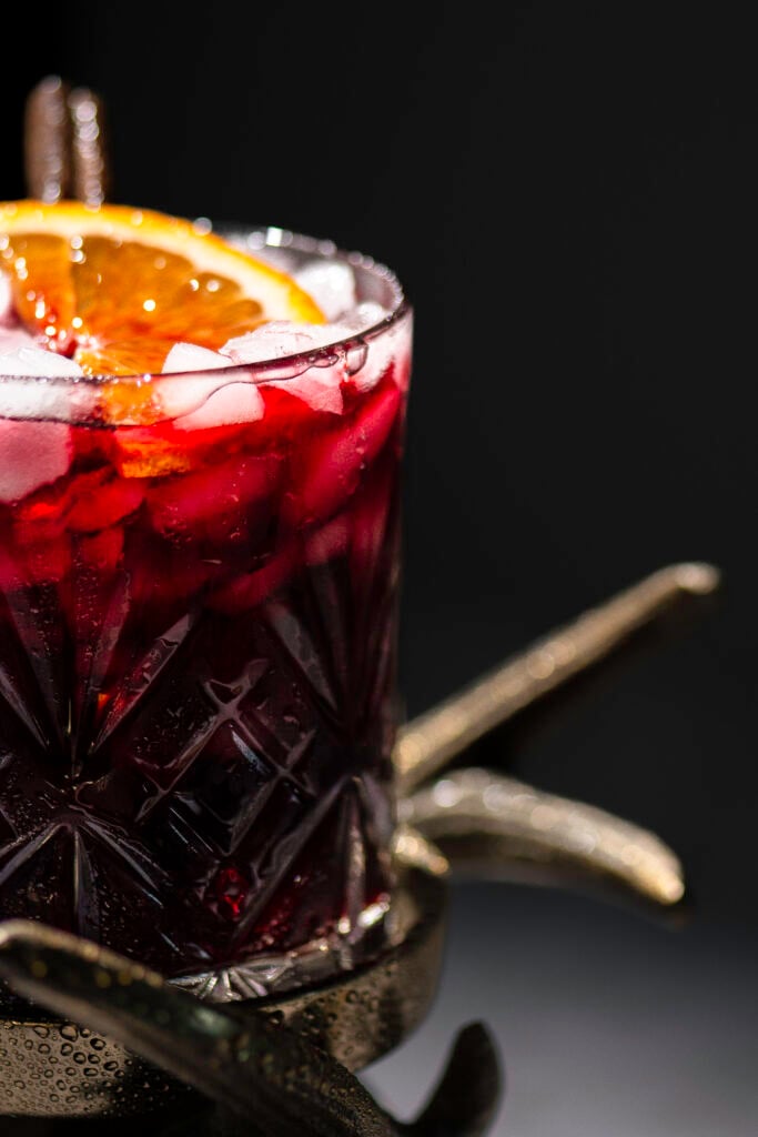 closeup of a glass of Jamaican sorrel drink garnished with a slice of orange and cinnamon stick in glass