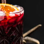 glass of Jamaican sorrel drink garnished with a slice of orange and cinnamon stick.