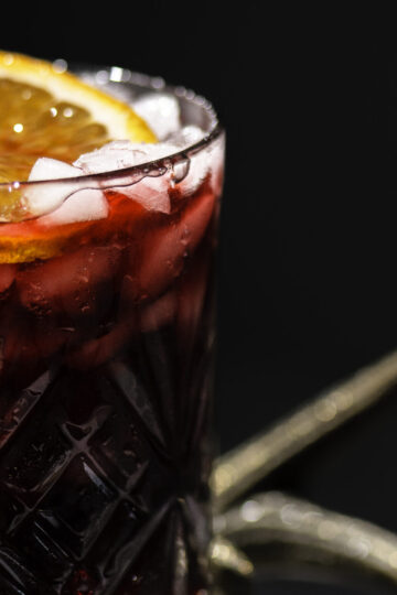 glass of Jamaican sorrel drink garnished with a slice of orange and cinnamon stick.