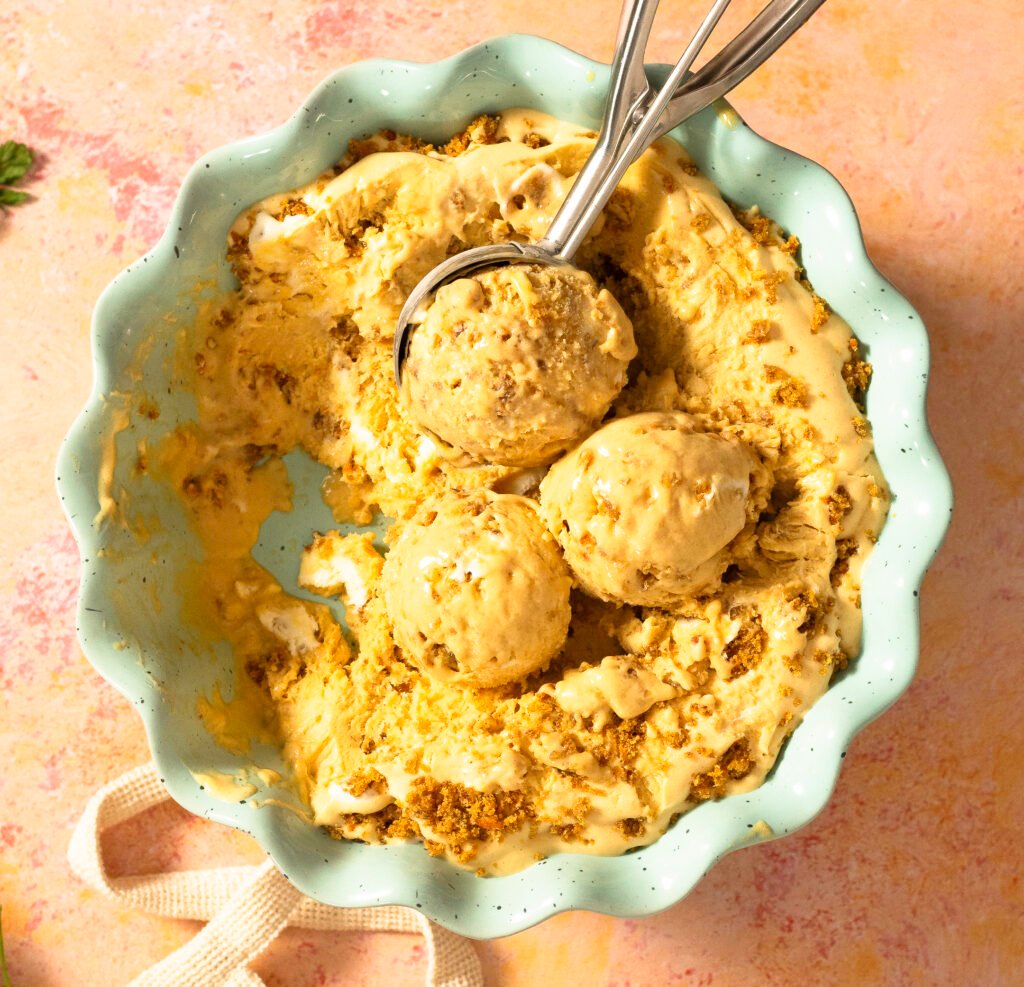 carrot cake ice cream with carrot cake crumbles and swirls of cream cheese frosting in a dish being scooped