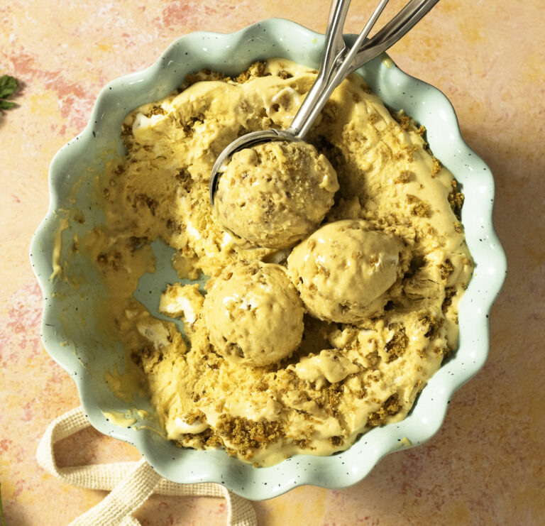 carrot cake ice cream with carrot cake crumbles and swirls of cream cheese frosting in a dish being scooped