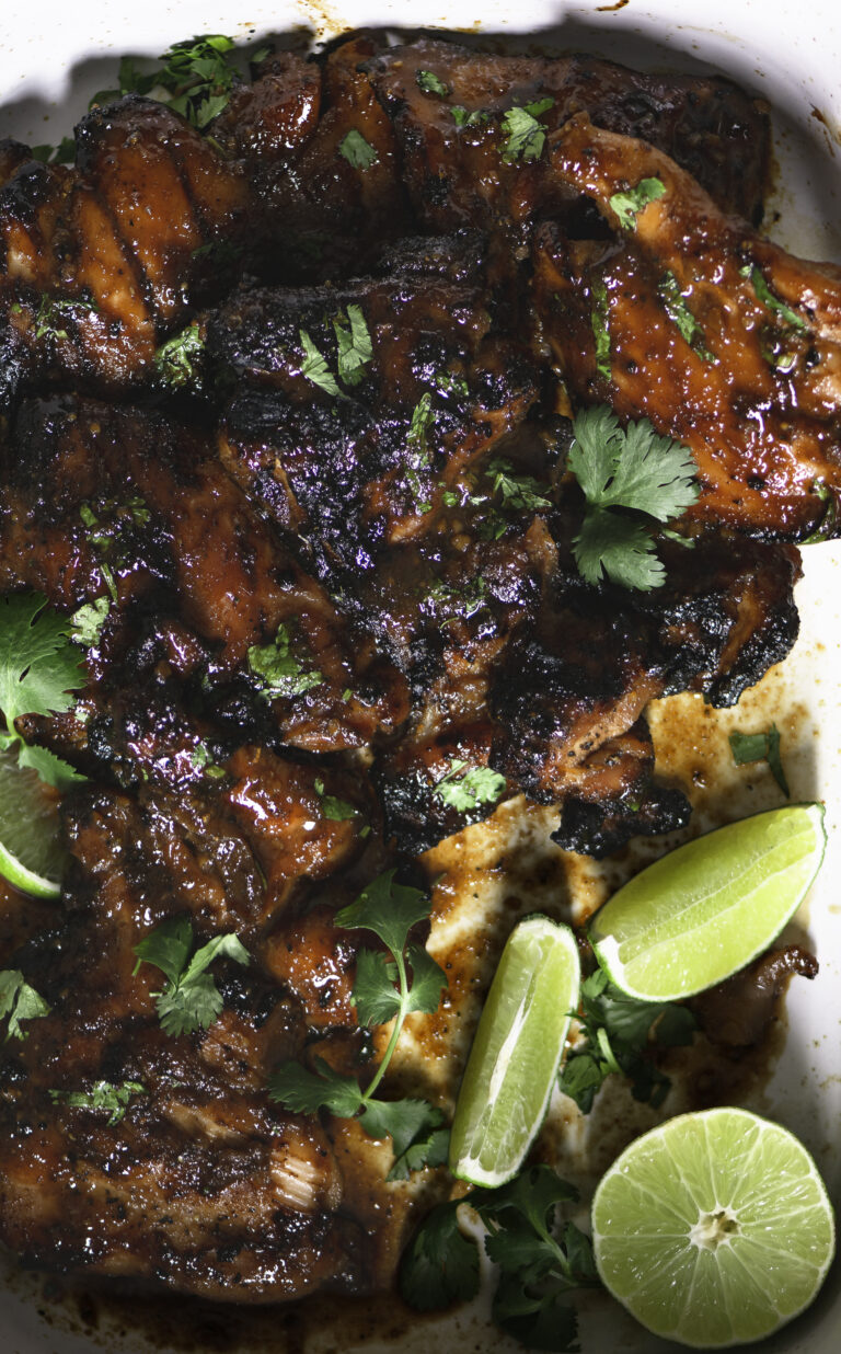 pan with charred grilled chicken thighs with honey-lime soy sauce glaze and garnished with lime wedges leaves of cilantro