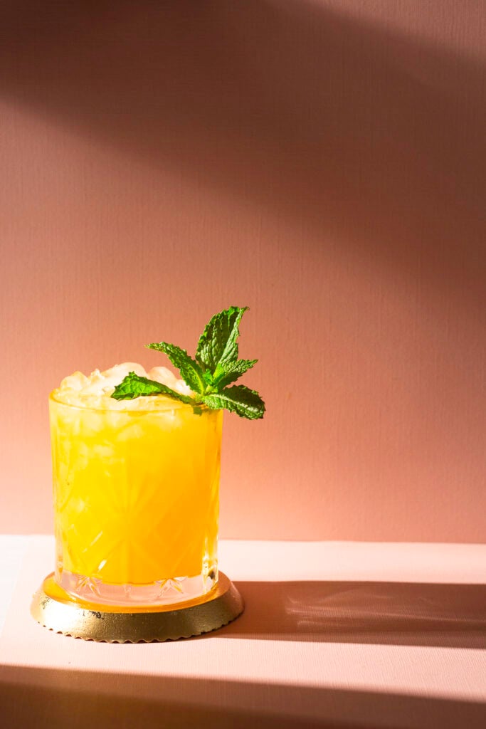 passion fruit gin & juice cocktail sitting on a gold coaster garnished with handful of mint