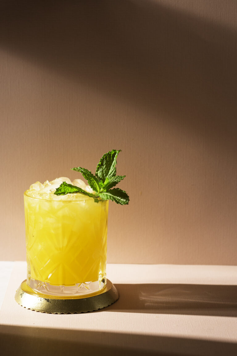 passion fruit gin & juice cocktail sitting on a gold coaster garnished with handful of mint