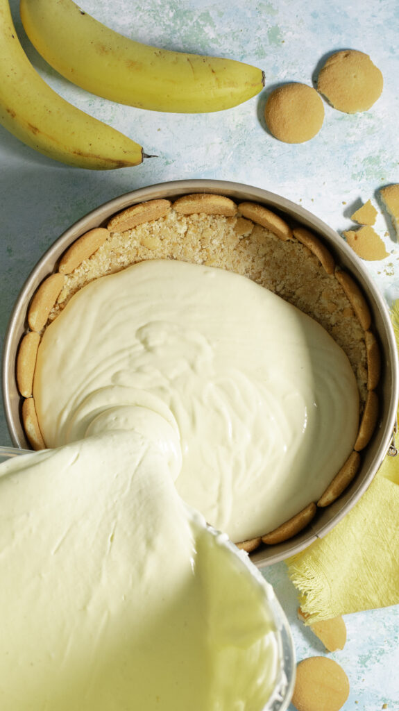 banana pudding cheesecake batter being poured into springform pan lined with whole Nilla wafers & Nilla wafer crust