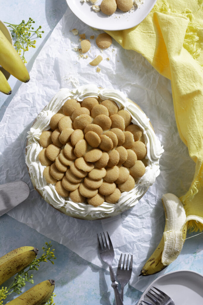 banana pudding cheesecake with whipped cream and Nilla wafers on parchment paper
