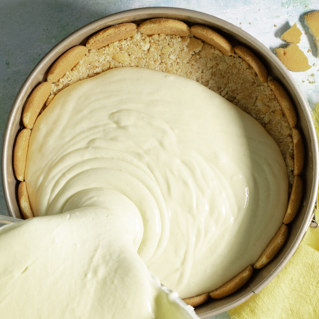 banana pudding cheesecake batter being poured into a springform pan lined with whole Nilla wafers and a Nilla wafer crust