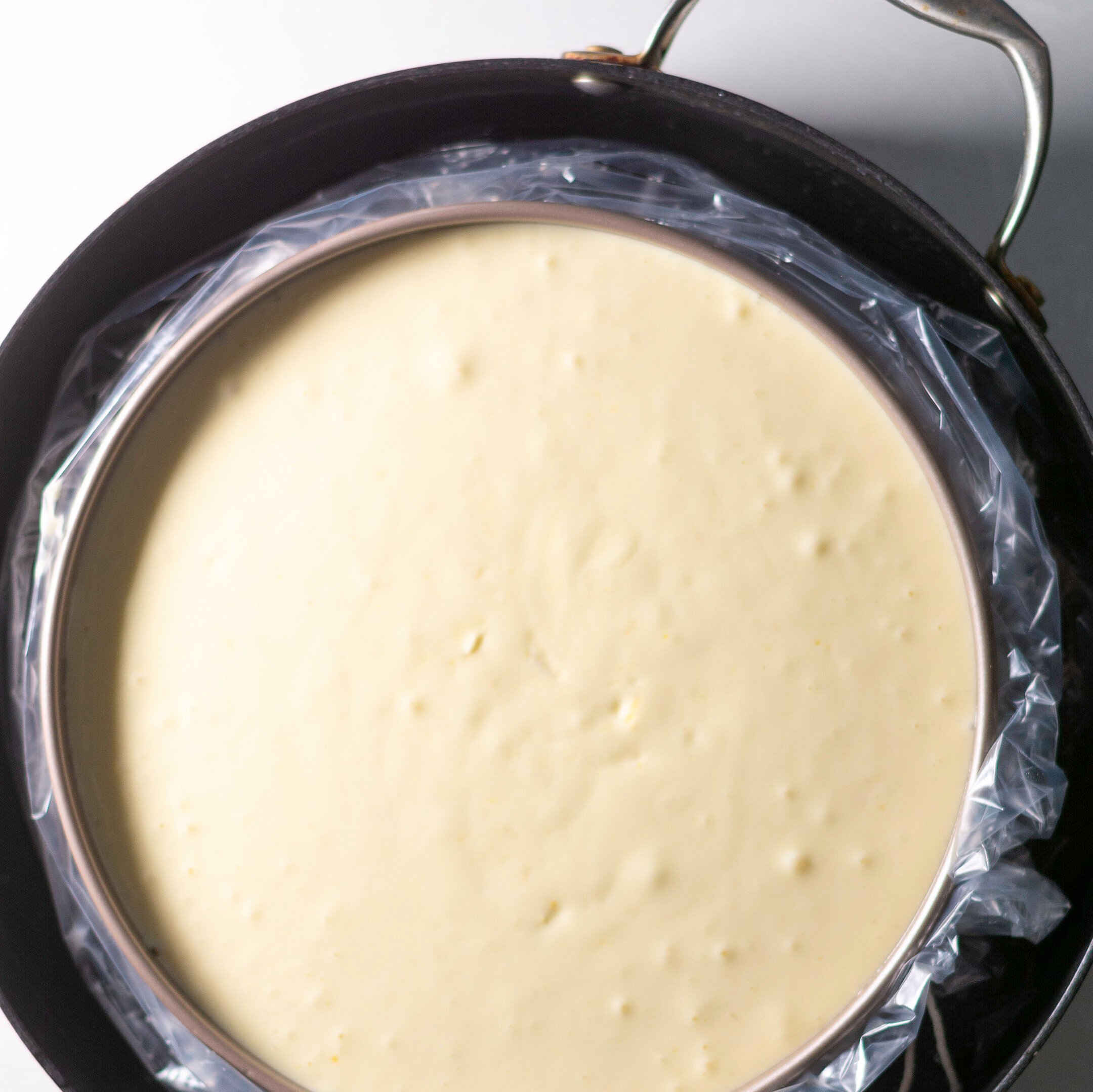 springform pan with lemon cheesecake filling in a water bath protected by oven bag