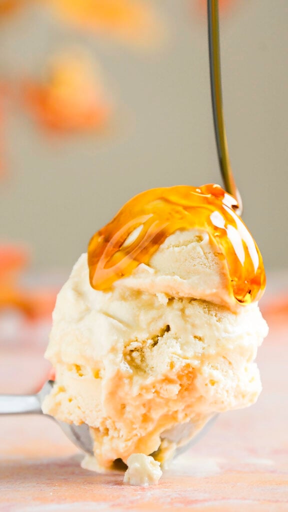 double scoop of salted maple custard ice cream in an ice cream scooper being drizzled with maple syrup