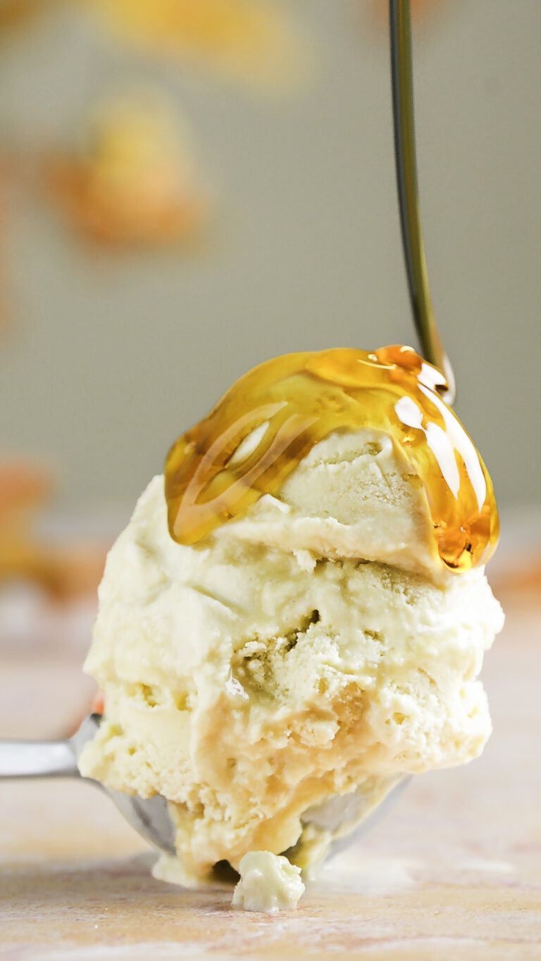 double scoop of salted maple custard ice cream in an ice cream scooper being drizzled with maple syrup