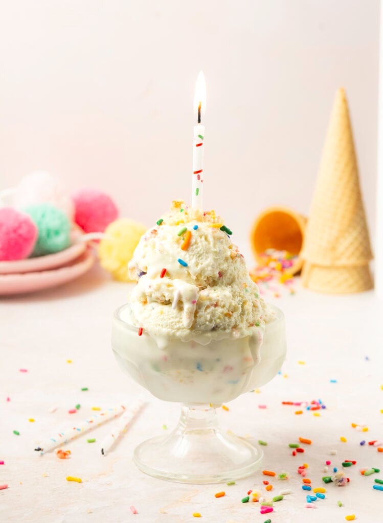 bowl of two scoops of funfetti birthday cake ice cream with a lit candle on top