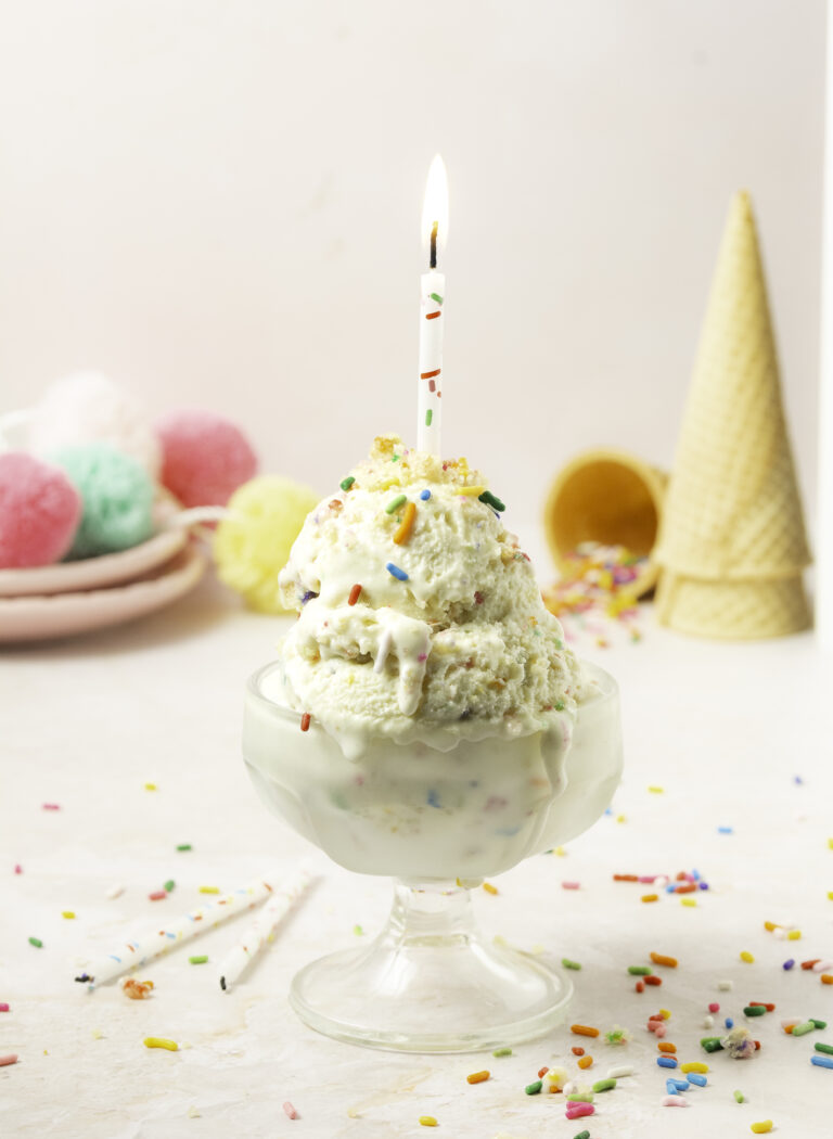bowl of two scoops of funfetti birthday cake ice cream with a lit candle on top