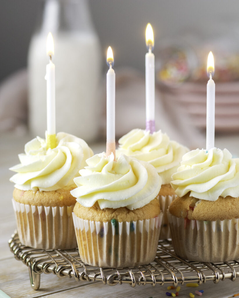 4 funfetti birthday cupcakes with one lit candle in each