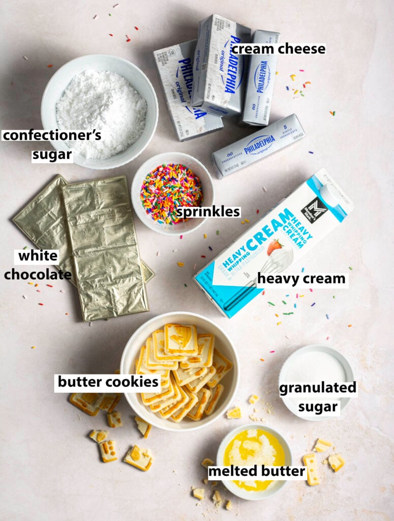 ingredients for no-bake white chocolate funfetti cheesecake - cream cheese, sprinkle jimmies, confectioner's sugar, white chocolate, Chessmen butter cookies, heavy whipping cream, granulated sugar, melted butter