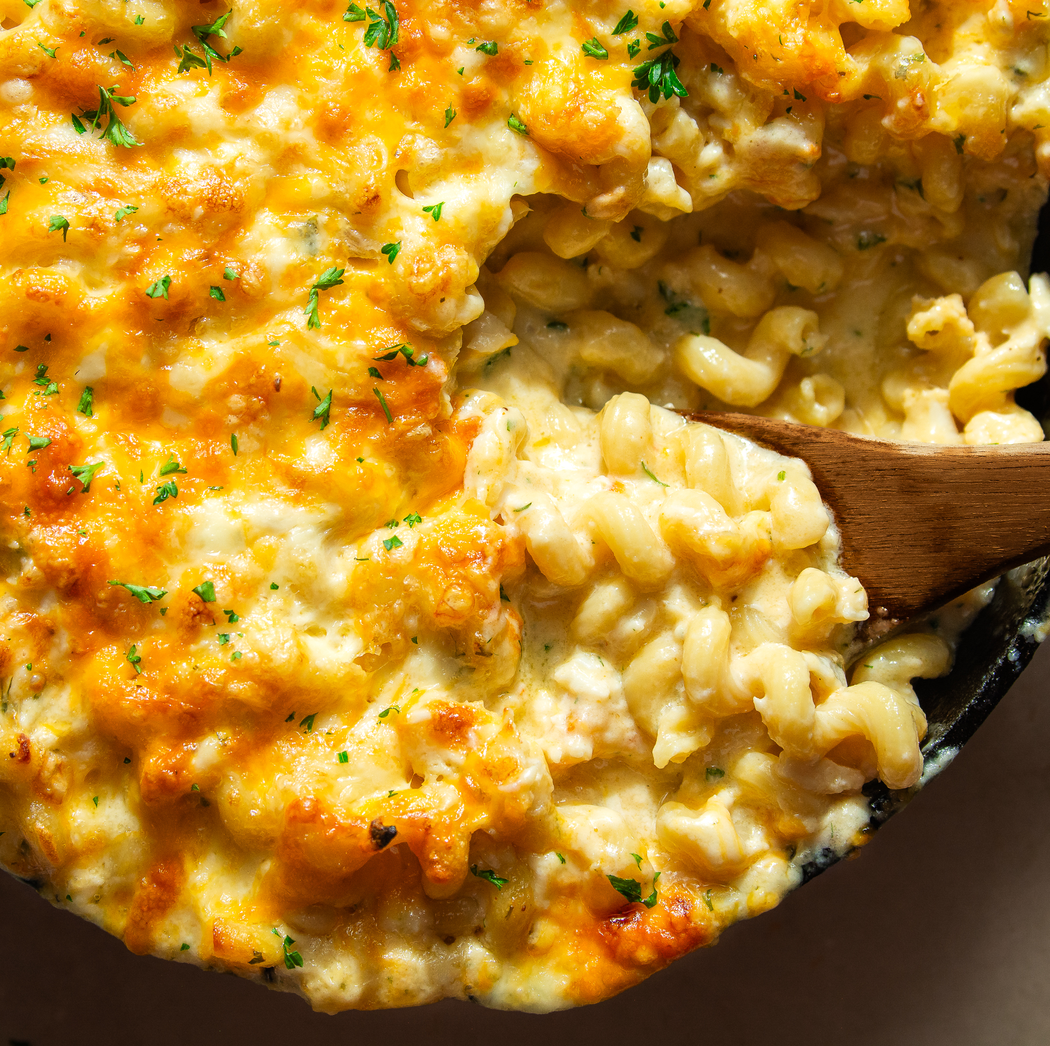 close up of crab macaroni and cheese in a lodge cast iron pan and a wooden spoon scooping a serving