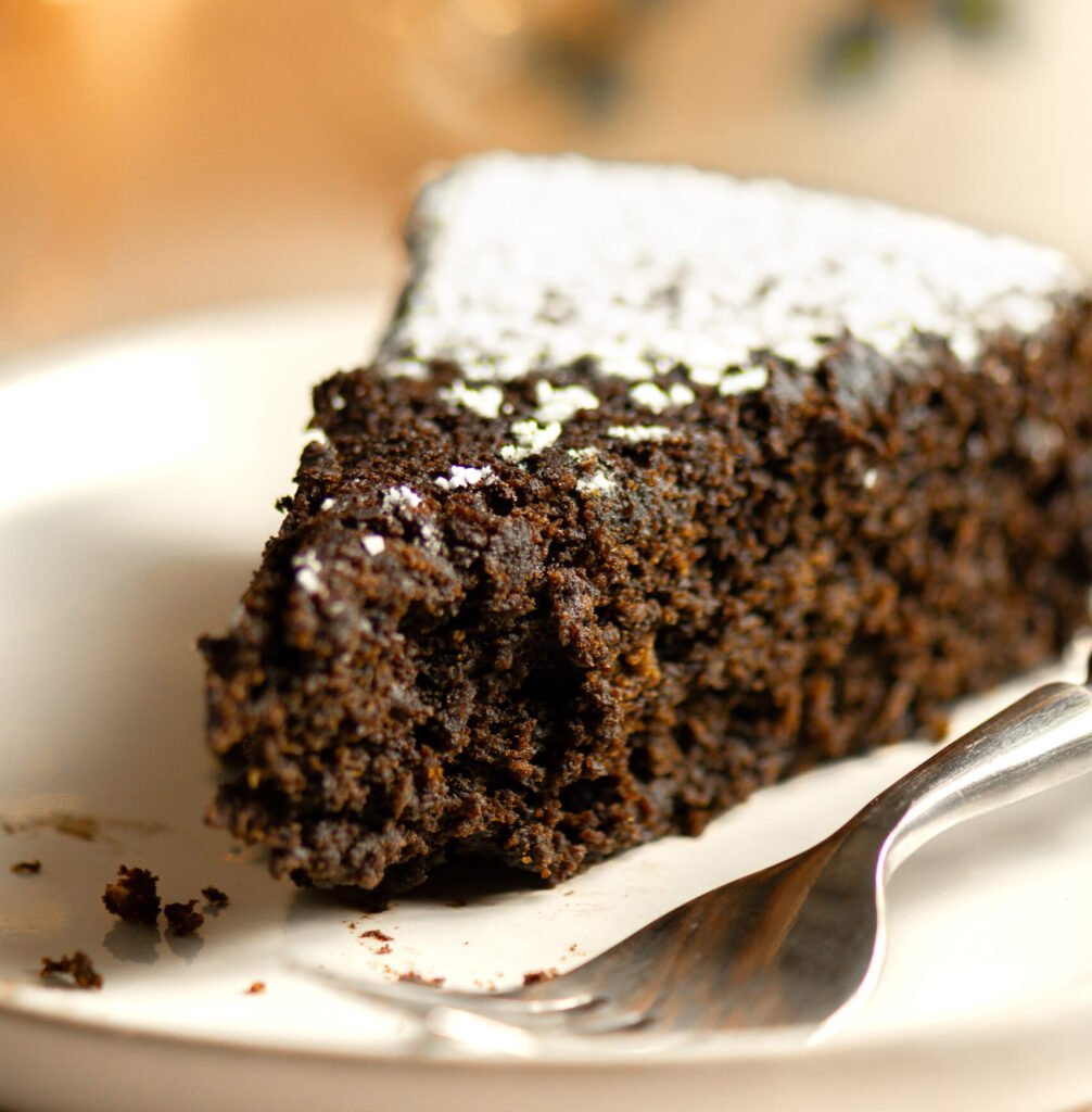 slice of Jamaican black cake with confectioner's sugar dusting on a white plate with a fork