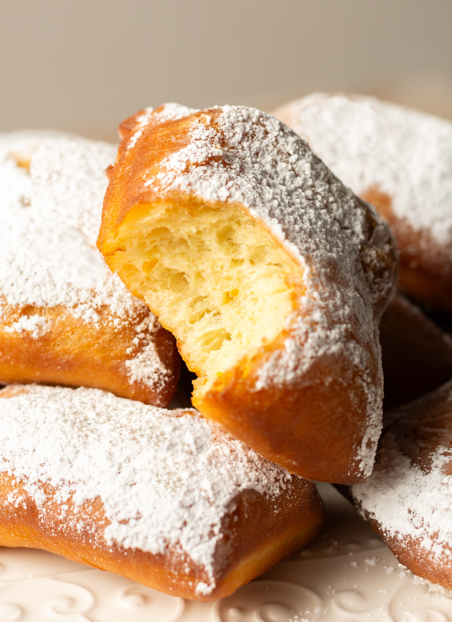 pile of beignets dusted with powdered sugar and one beignet missing a bite