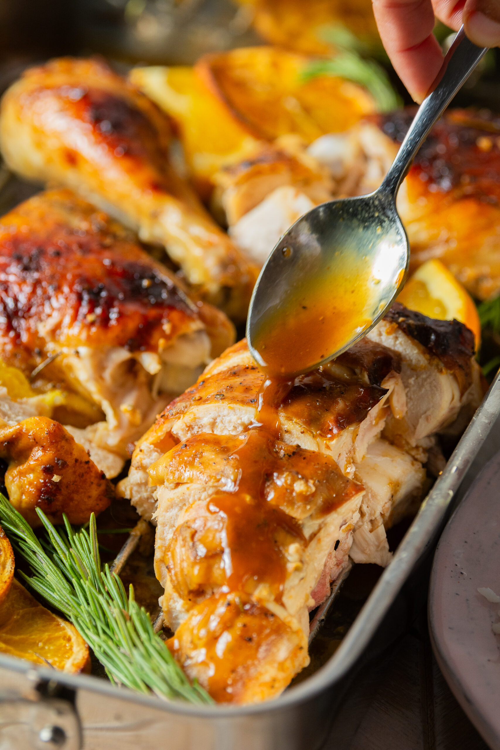 spooning orange maple glaze over spatchcocked and whole roasted orange maple chicken