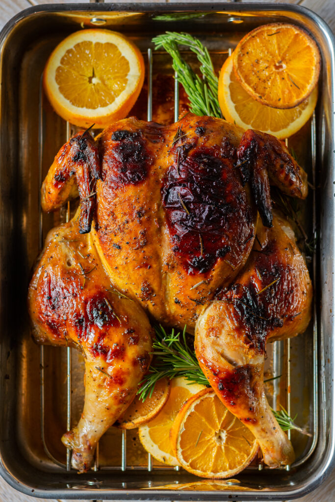 spatchcocked and whole roasted orange maple chicken on a rack in a roasting pan