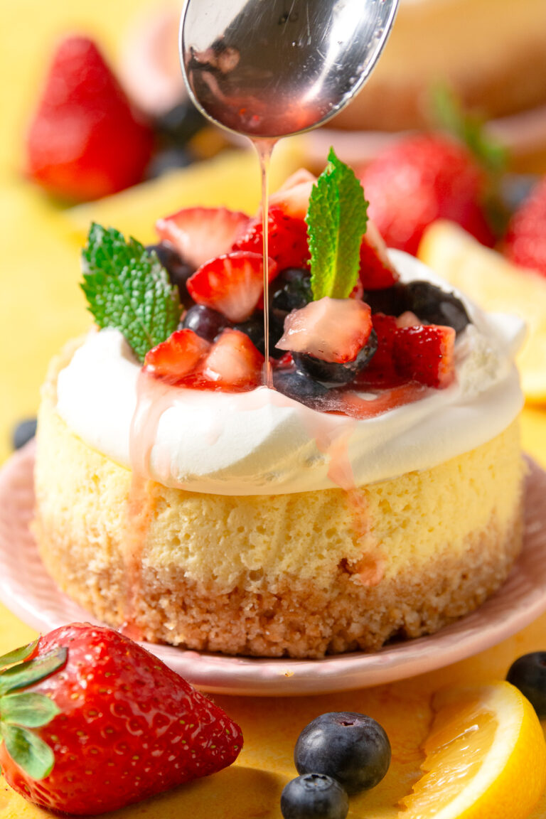 baked mini lemon cheesecake topped with cool whip & fresh macerated berries on a pink plate