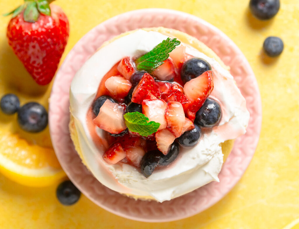 baked mini lemon cheesecake topped with cool whip & fresh macerated berries on a pink plate