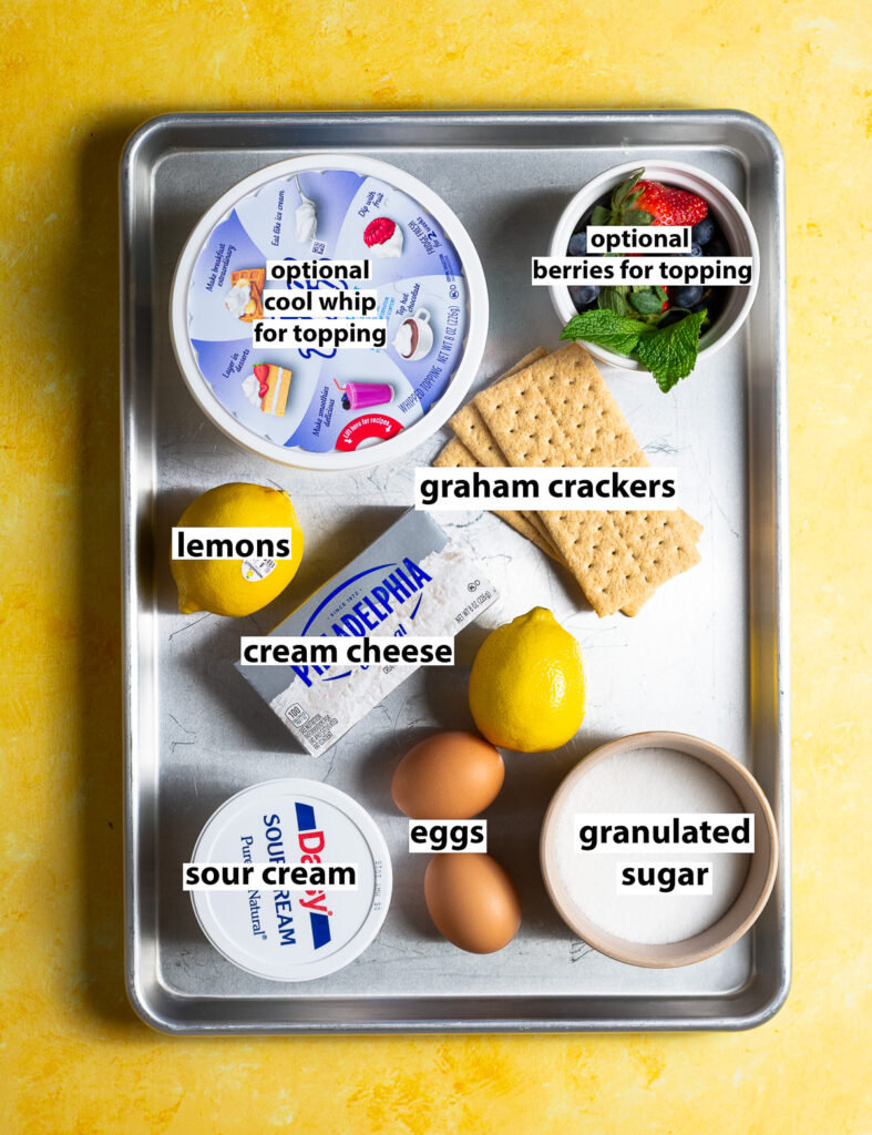 ingredients for air fruer mini lemon cheesecakes - cream cheese, lemons, sour cream, eggs, granulated sugar, graham crackers, butter, optional cool whip for topping & optional berries for topping