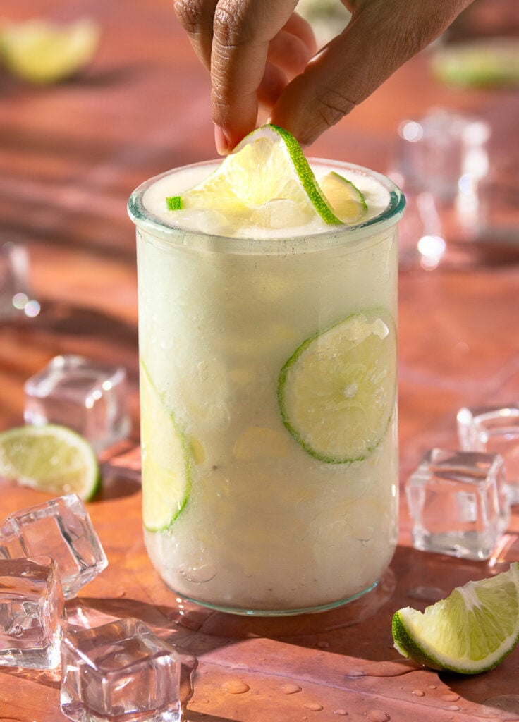 hand placing a slice of lime on top of a glass of Jamaican soursop juice