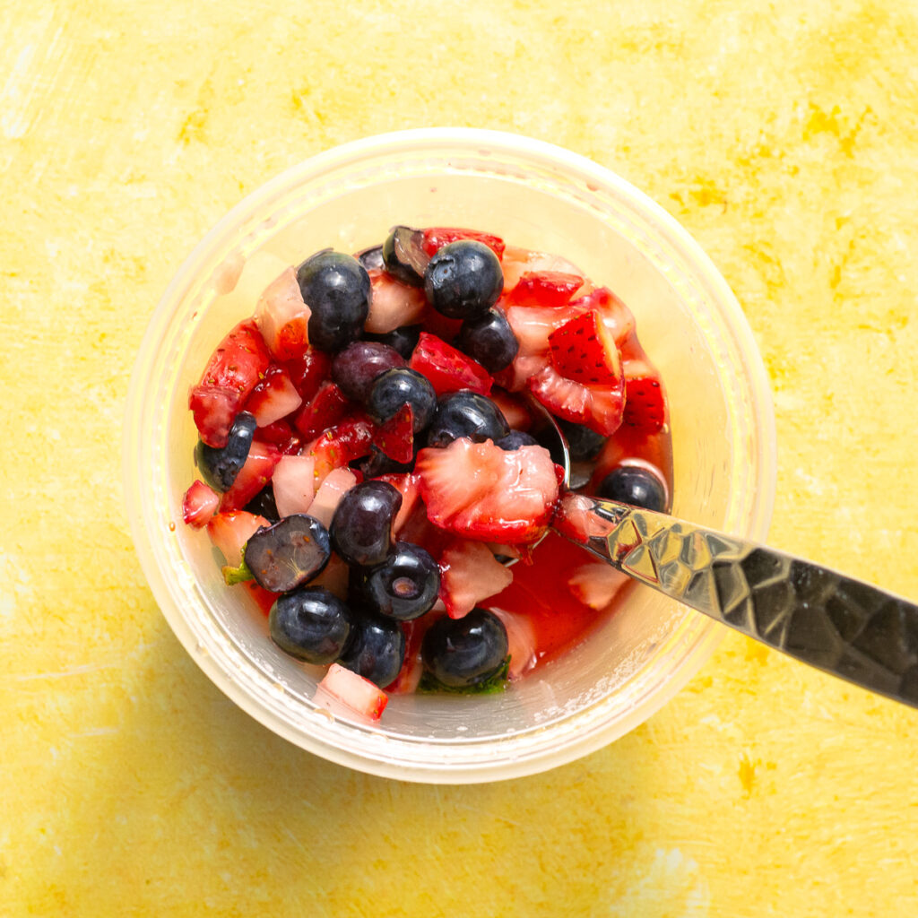 macerated sliced strawberries and halved blueberries with mint leaves in a container