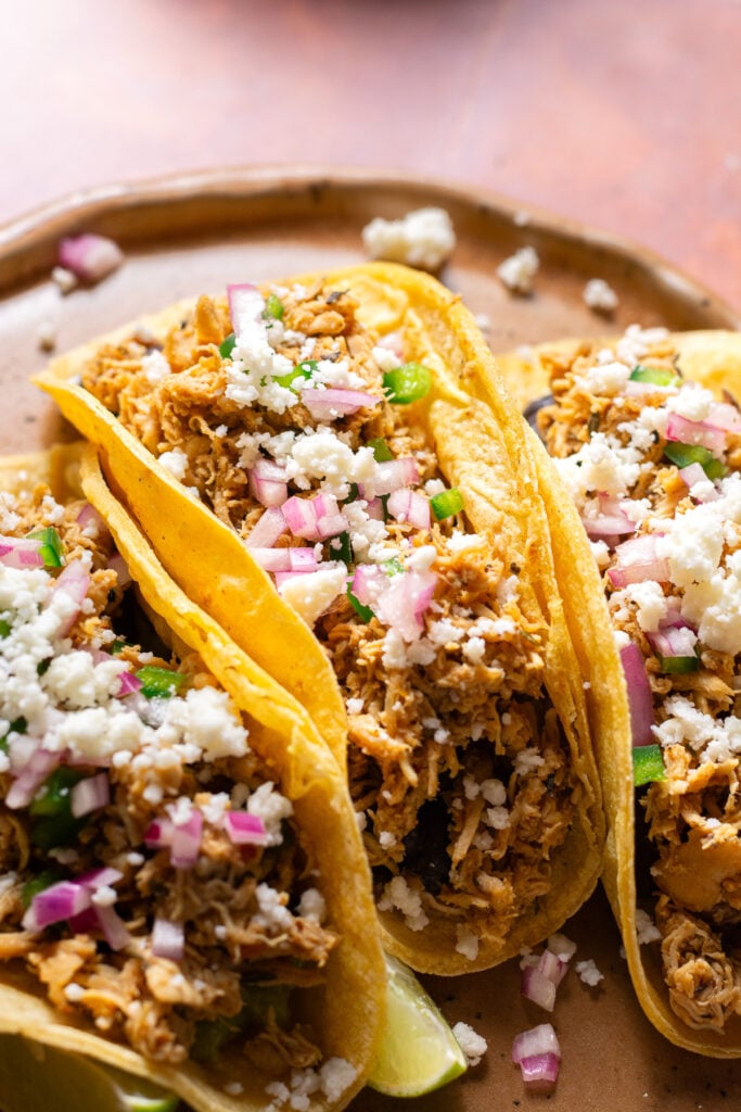 three chicken tinga tacos on a plate with lime wedges