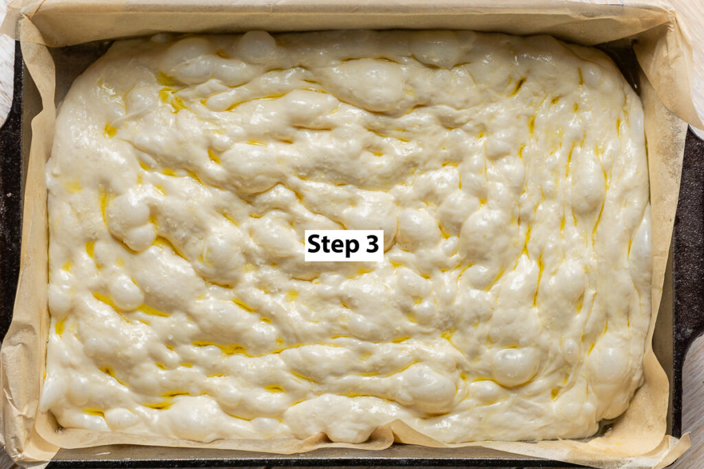 dimpled cassava focaccia dough in a cast iron pan lined with parchment paper
