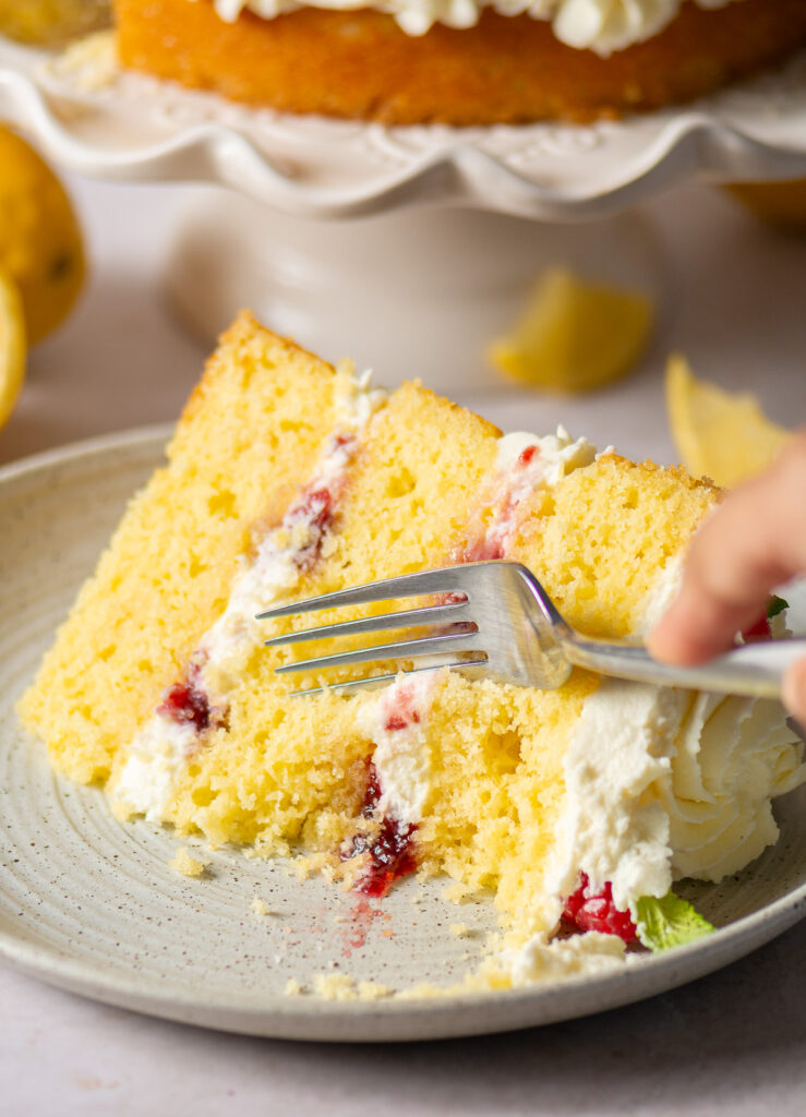 a slice of a 3-layer honey lemon cake showing mascarpone whipped cream and raspberry preserve filling