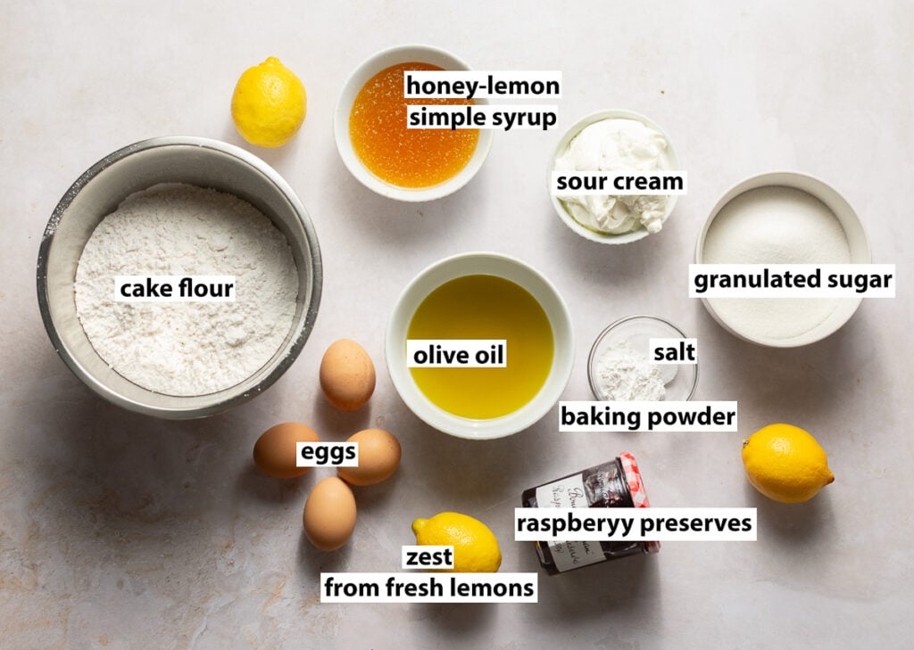 ingredients for honey lemon layer cake - cake flour, lemon zest from fresh lemons, olive oil, eggs, baking powder, salt, granulated sugar, honey lemon simple syrup and raspberry preserves for filling