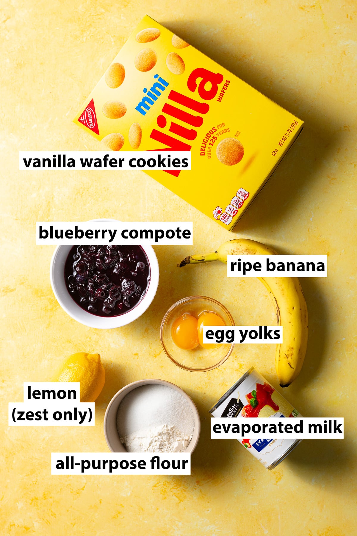 ingredients for lemon-blueberry banana pudding - ripe banana, vanilla wafer cookies, lemon zest, blueberry compote, egg yolks, evaporated milk, sugar & all-purpose flour.