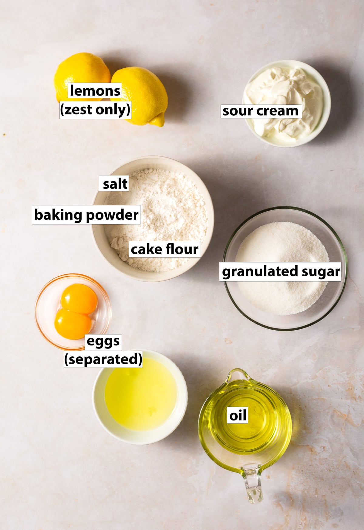 ingredients for lemon cupcakes - lemon zest, sour cream, cake flour, eggs (separated), oil, baking powder, salt.