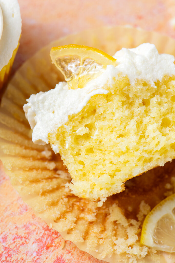 close up of a lemon cupcake with ermine cream cheese frosting cut in half