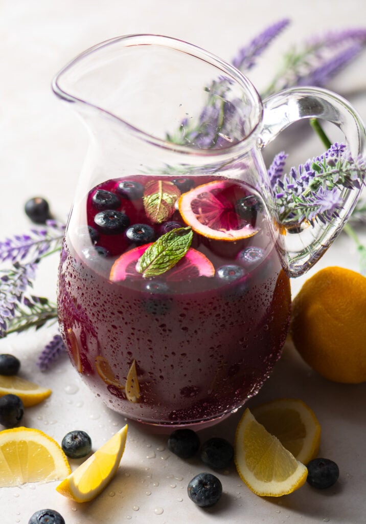 pitcher of blueberry lavender lemonade garnished with a couple of mint leaves blueberries and lemon slices