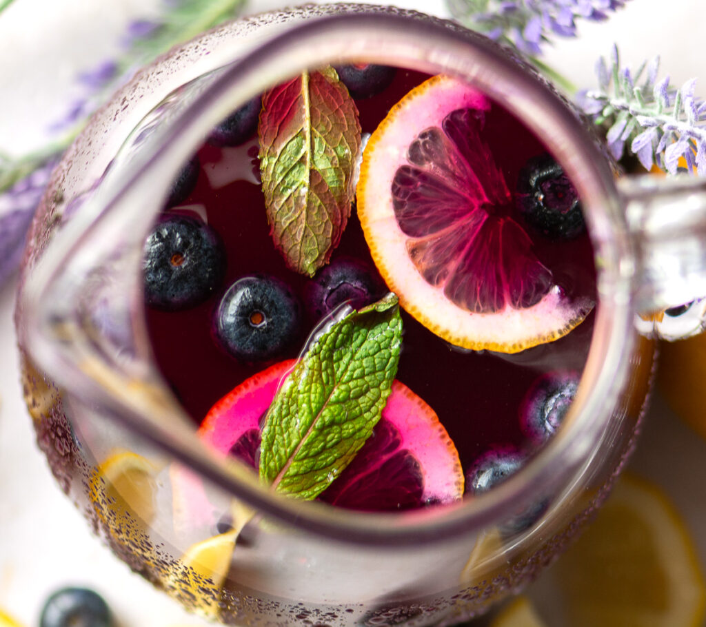 pitcher of blueberry lavender lemonade garnished with a couple of mint leaves blueberries and lemon slices