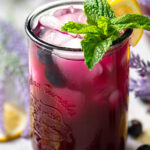 glass of blueberry lavender lemonade garnished with a sprig of mint and a lemon wedge
