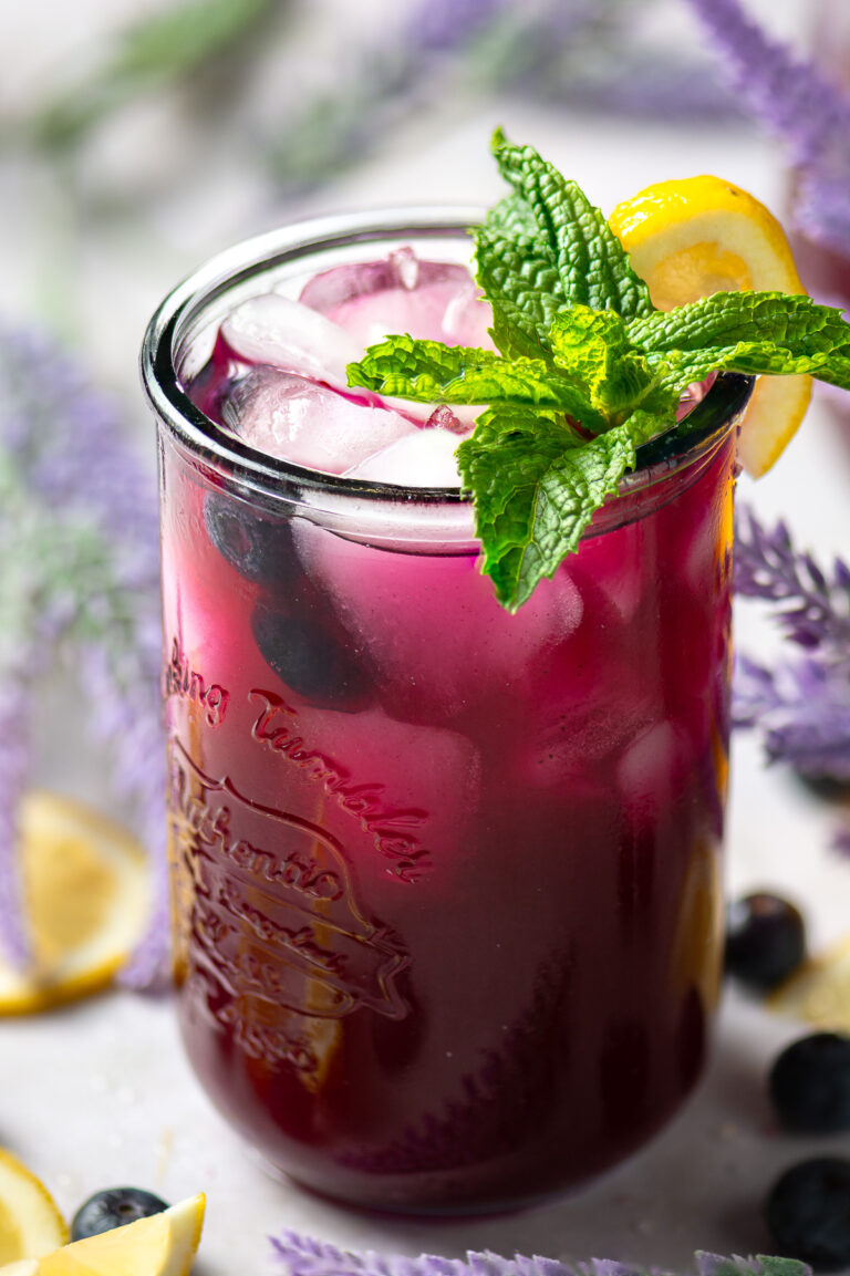 glass of blueberry lavender lemonade garnished with a sprig of mint and a lemon wedge.