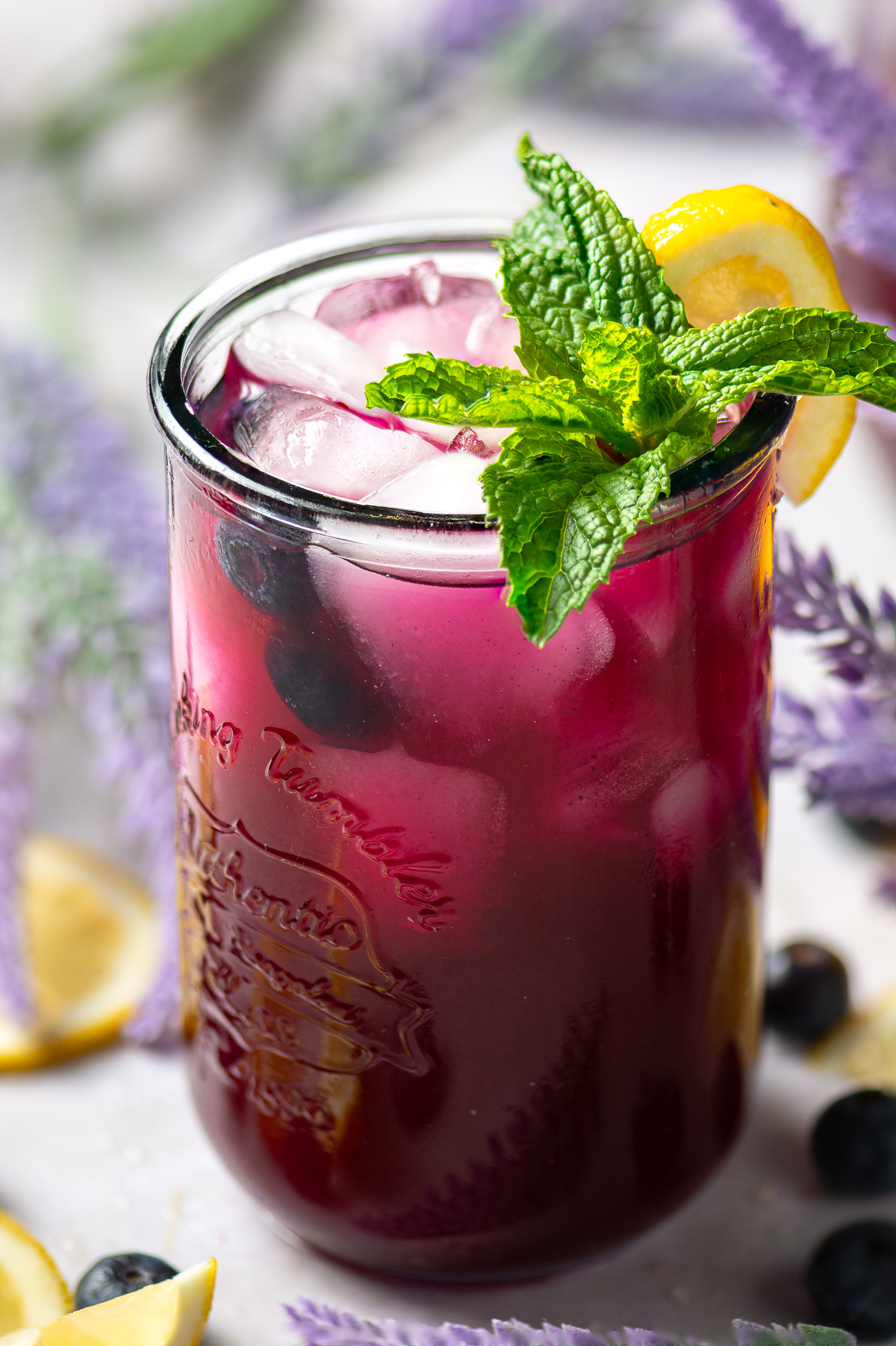 glass of blueberry lavender lemonade garnished with a sprig of mint and a lemon wedge