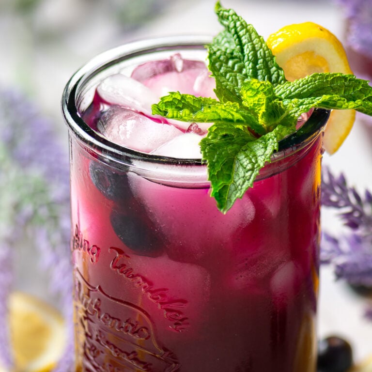 glass of blueberry lavender lemonade garnished with a sprig of mint and a lemon wedge.