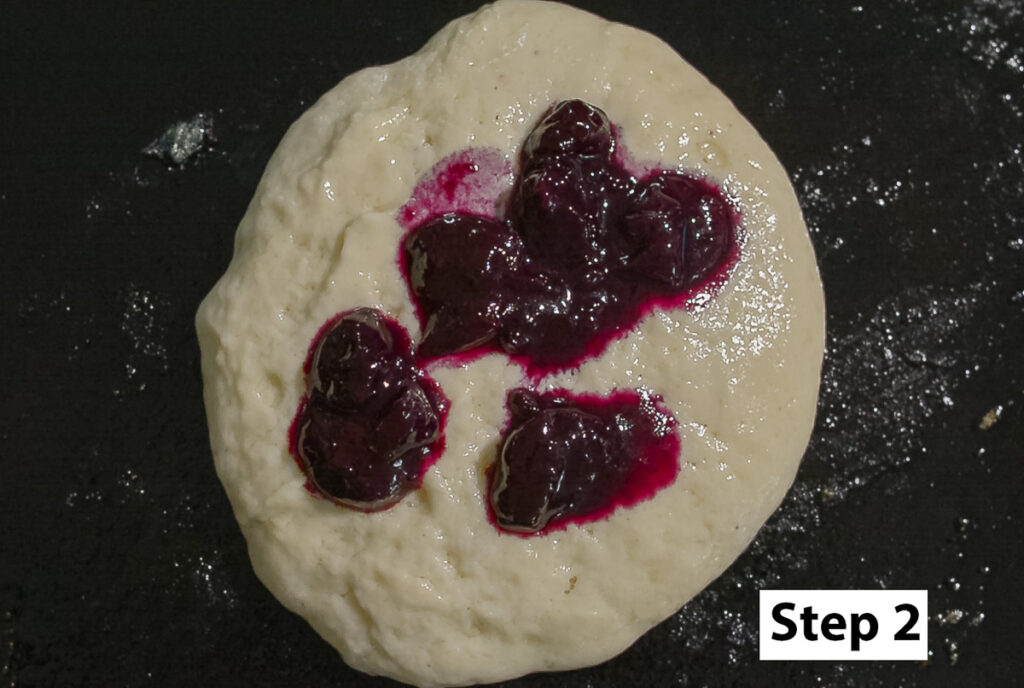 pancake batter on a cast iron griddle with dollops of blueberry compote