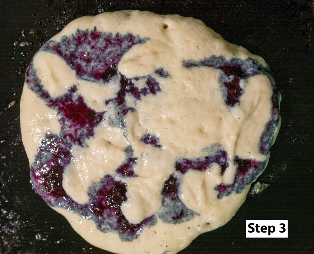 homemade blueberry pancake on a cast iron griddle before flipping