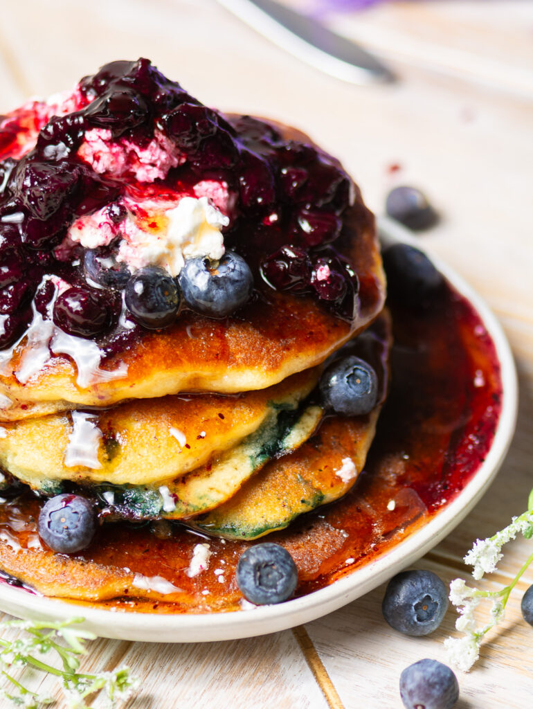 stack of homemade blueberry pancakes on a plate topped with fresh blueberry compote & cool whip