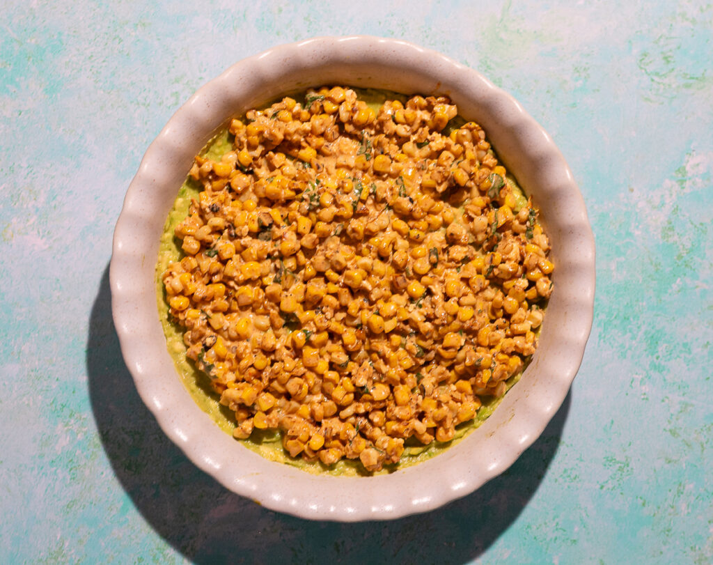 layering a mexican dip in a pie dish with corn esquites